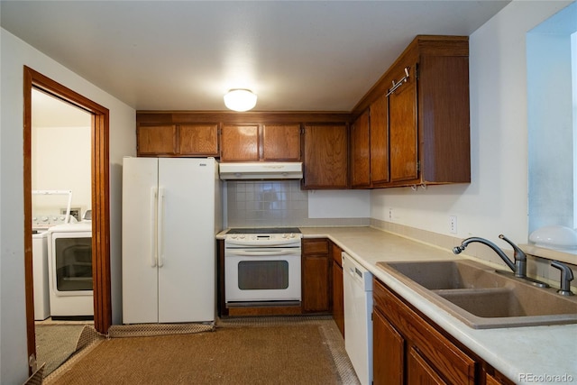 kitchen with under cabinet range hood, white appliances, a sink, brown cabinets, and washing machine and clothes dryer