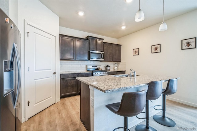 kitchen with sink, stainless steel appliances, light hardwood / wood-style flooring, decorative light fixtures, and a kitchen island with sink