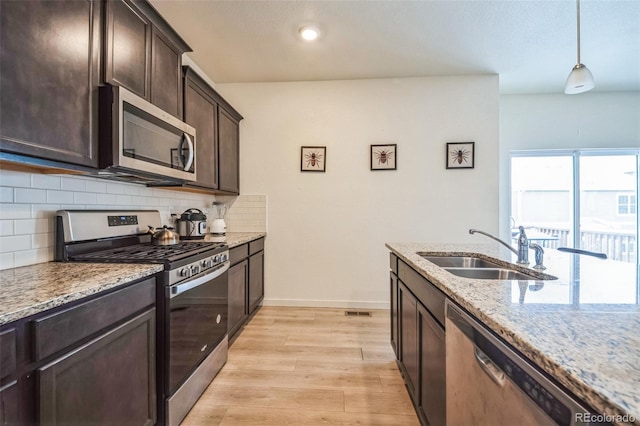 kitchen featuring light stone counters, stainless steel appliances, sink, light hardwood / wood-style flooring, and hanging light fixtures