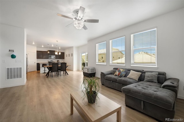 living room with ceiling fan with notable chandelier and light hardwood / wood-style flooring