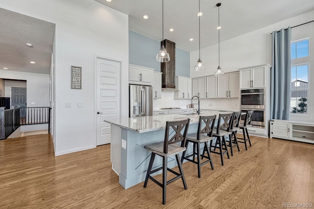 kitchen with white cabinets, decorative light fixtures, a towering ceiling, appliances with stainless steel finishes, and a large island