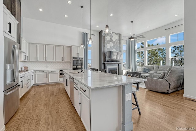 kitchen featuring a center island with sink, decorative backsplash, light stone countertops, appliances with stainless steel finishes, and white cabinetry