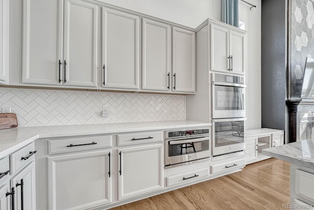 kitchen featuring stainless steel double oven, light stone countertops, light wood-type flooring, tasteful backsplash, and white cabinetry