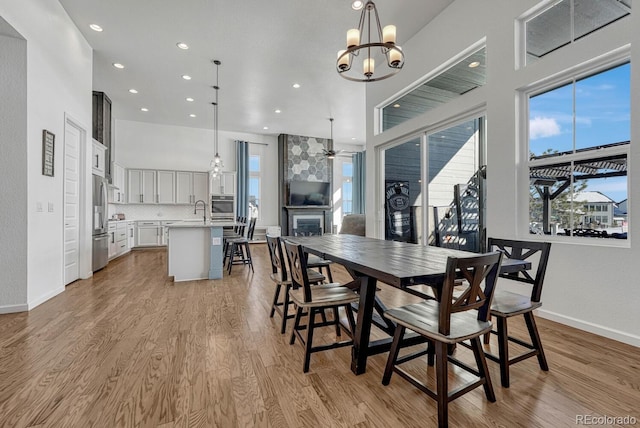 dining room featuring a fireplace, ceiling fan with notable chandelier, light hardwood / wood-style flooring, and sink