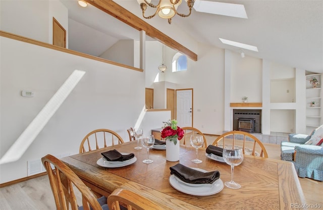 dining space with built in shelves, an inviting chandelier, a tiled fireplace, wood finished floors, and a skylight