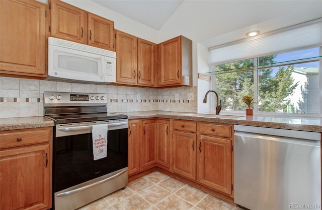 kitchen with appliances with stainless steel finishes, vaulted ceiling, light stone countertops, decorative backsplash, and a sink