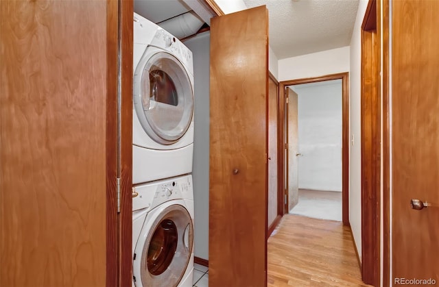 clothes washing area featuring stacked washer / dryer, laundry area, a textured ceiling, and light wood-style flooring