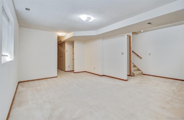 finished basement featuring baseboards, light carpet, a textured ceiling, stairs, and visible vents