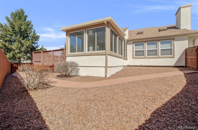rear view of house with a sunroom, a fenced backyard, stucco siding, a chimney, and a deck