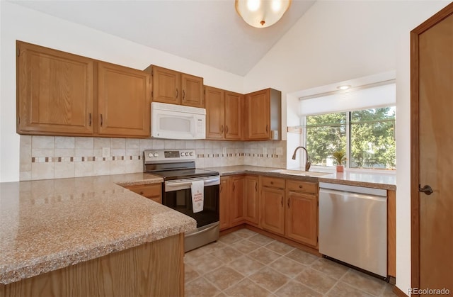 kitchen featuring vaulted ceiling, light countertops, decorative backsplash, stainless steel appliances, and a sink