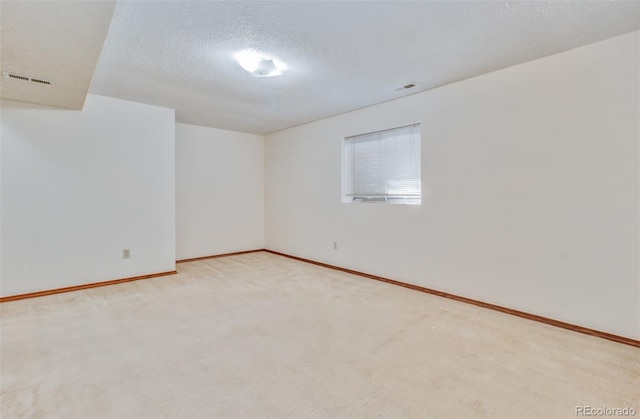 spare room with baseboards, visible vents, a textured ceiling, and light colored carpet
