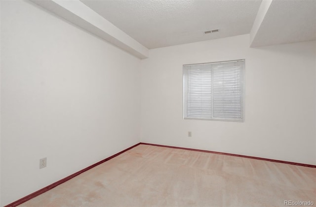 carpeted spare room with visible vents, baseboards, and a textured ceiling