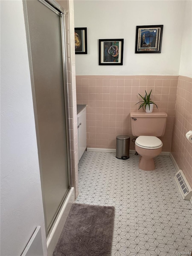 bathroom featuring toilet, a shower with shower door, tile walls, tile patterned flooring, and vanity