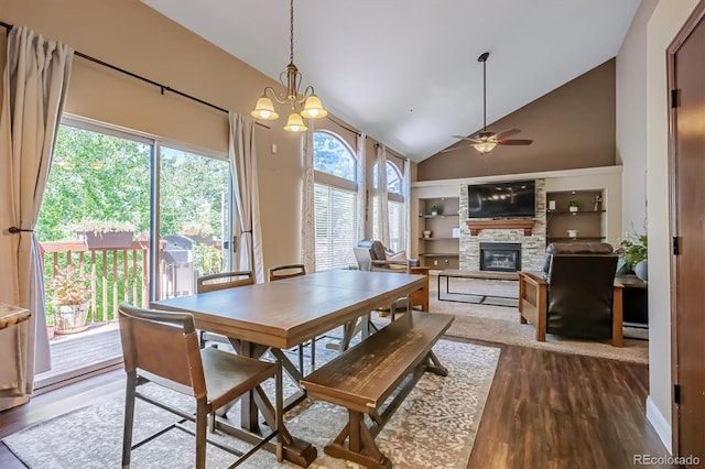 dining area featuring high vaulted ceiling, ceiling fan with notable chandelier, wood-type flooring, and a stone fireplace