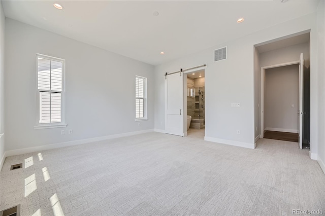 unfurnished bedroom with light colored carpet, ensuite bath, and a barn door