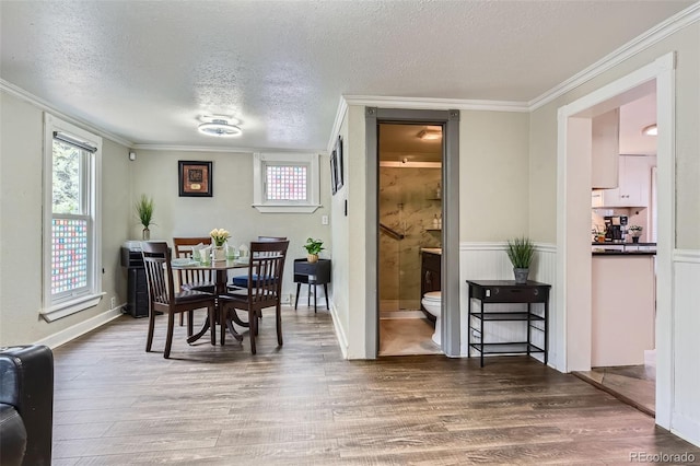 dining space featuring wood finished floors, a textured ceiling, ornamental molding, and baseboards