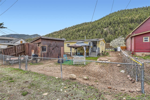 rear view of property featuring a mountain view, a gate, a fenced backyard, and a wooded view