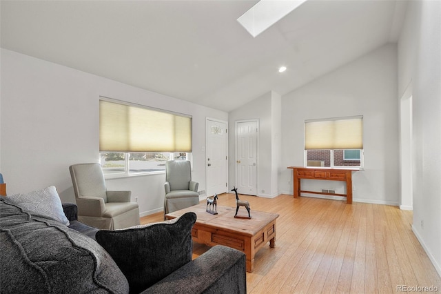 living room featuring light hardwood / wood-style flooring, high vaulted ceiling, and a skylight