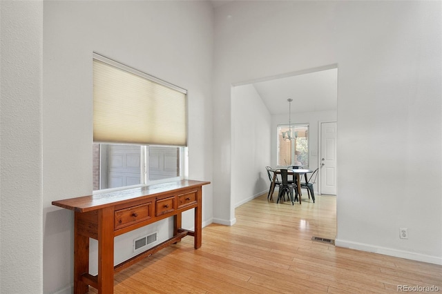 hall featuring visible vents, light wood-style flooring, baseboards, and a chandelier