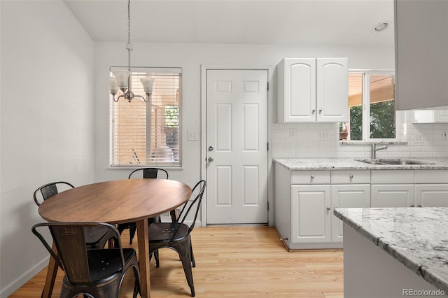 kitchen featuring light stone countertops, a chandelier, white cabinets, a sink, and backsplash