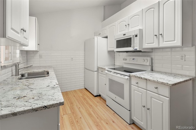 kitchen with white appliances, tile walls, light wood-style floors, white cabinets, and a sink