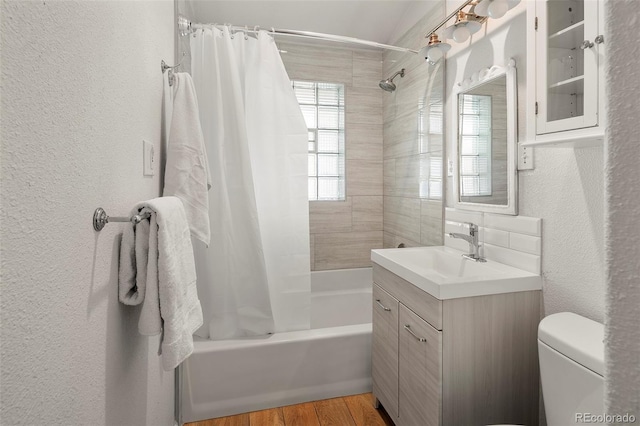 full bathroom featuring toilet, a textured wall, shower / bath combo, and vanity