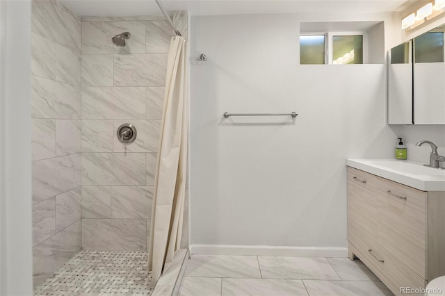 bathroom with baseboards, marble finish floor, a tile shower, and vanity
