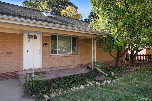 property entrance with brick siding, fence, and roof with shingles