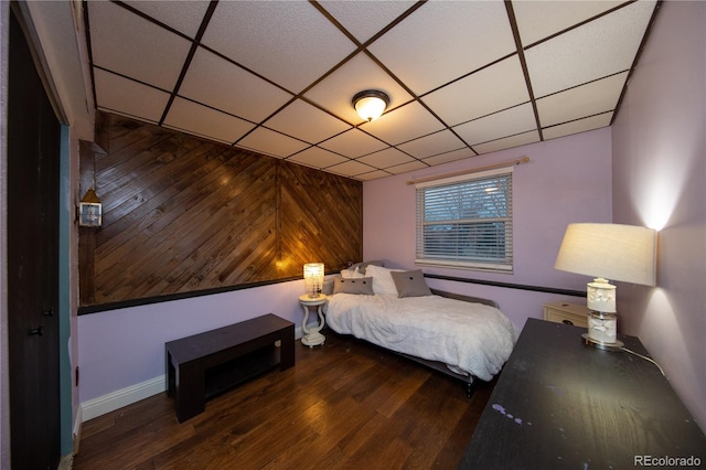 bedroom featuring a paneled ceiling, wooden walls, and hardwood / wood-style floors