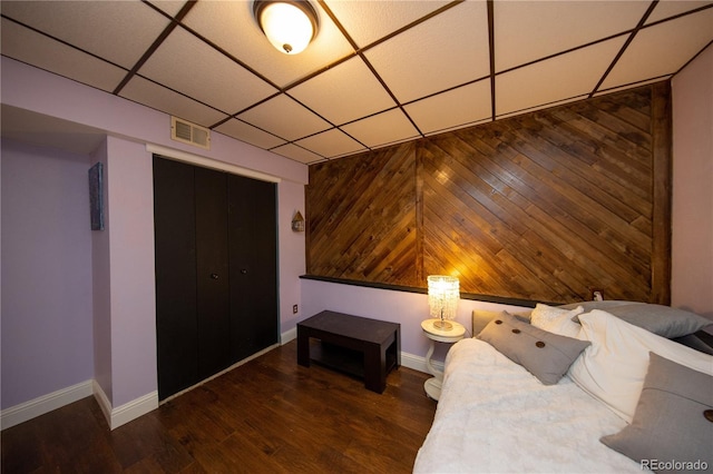 unfurnished bedroom featuring dark hardwood / wood-style floors, a paneled ceiling, wooden walls, and a closet