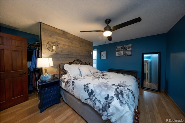 bedroom featuring ceiling fan, wooden walls, a textured ceiling, and light wood-type flooring