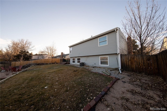 back house at dusk featuring a yard and central air condition unit