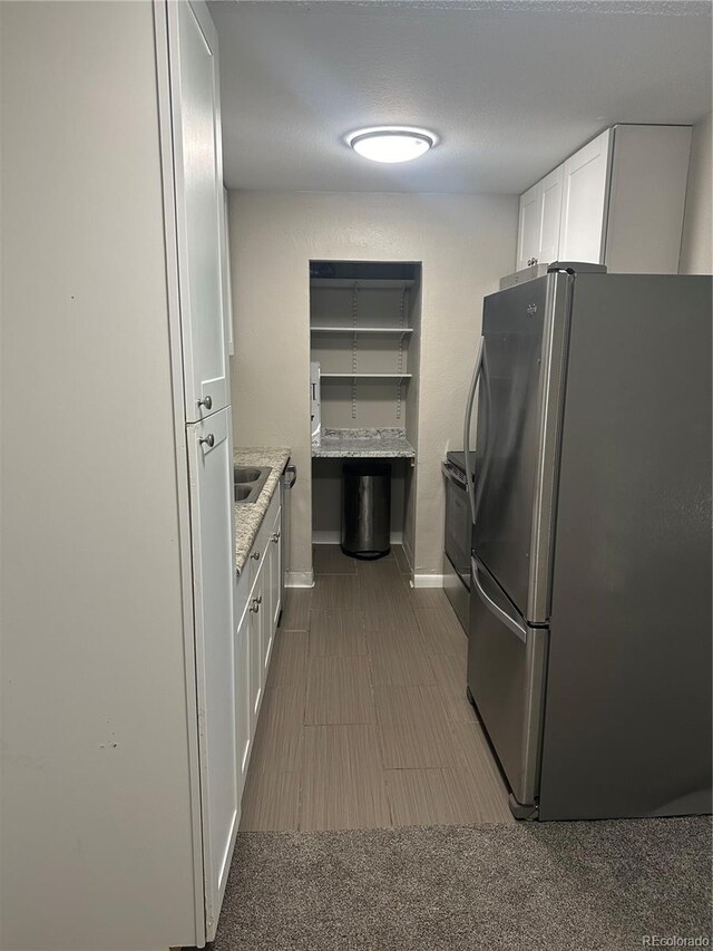 kitchen featuring white cabinets, light stone counters, appliances with stainless steel finishes, light colored carpet, and sink