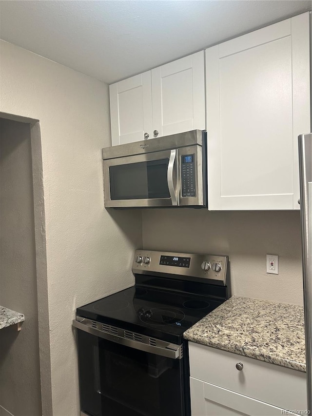 kitchen with appliances with stainless steel finishes, white cabinetry, and light stone counters