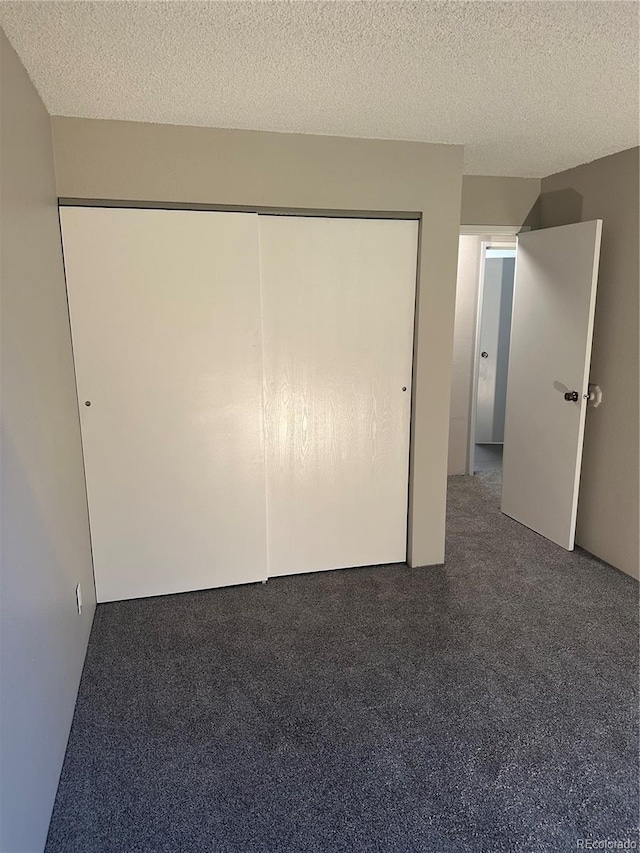 unfurnished bedroom with a closet, a textured ceiling, and dark carpet