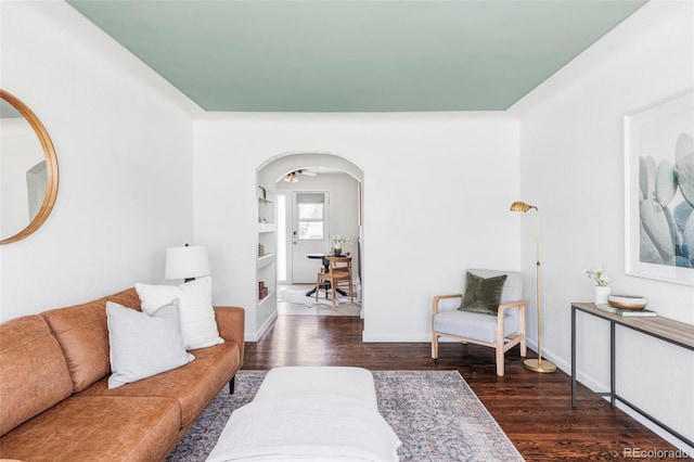 living area with arched walkways, dark wood-style flooring, and baseboards