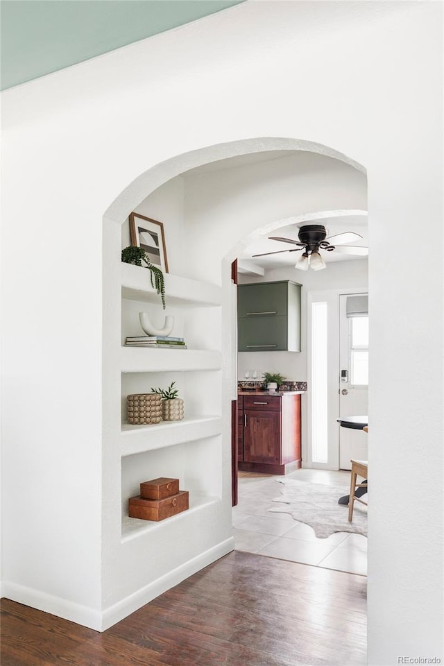 corridor with built in shelves, wood finished floors, baseboards, and arched walkways