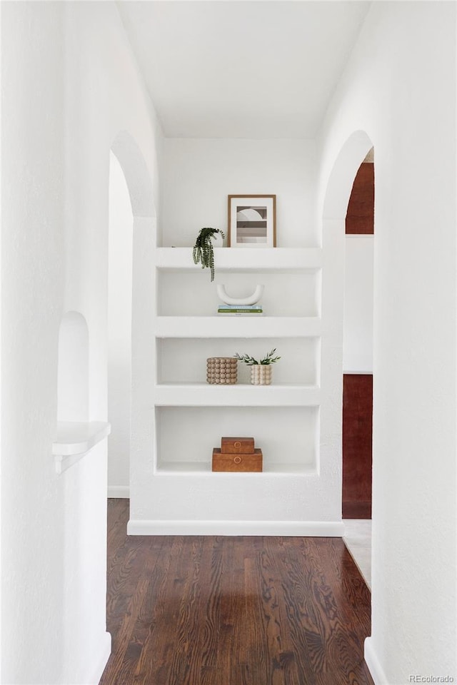 corridor with built in shelves, arched walkways, and wood finished floors