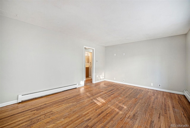 unfurnished room featuring a baseboard heating unit, baseboards, and wood finished floors