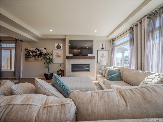 living area with plenty of natural light, a tiled fireplace, wood finished floors, and baseboards