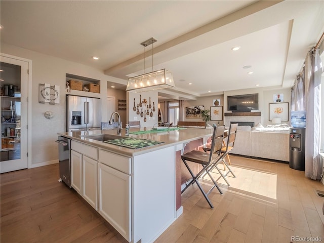 kitchen with white cabinetry, open floor plan, stainless steel fridge with ice dispenser, an island with sink, and pendant lighting