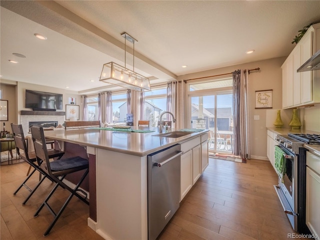 kitchen with white cabinets, decorative light fixtures, a kitchen island with sink, stainless steel appliances, and light countertops