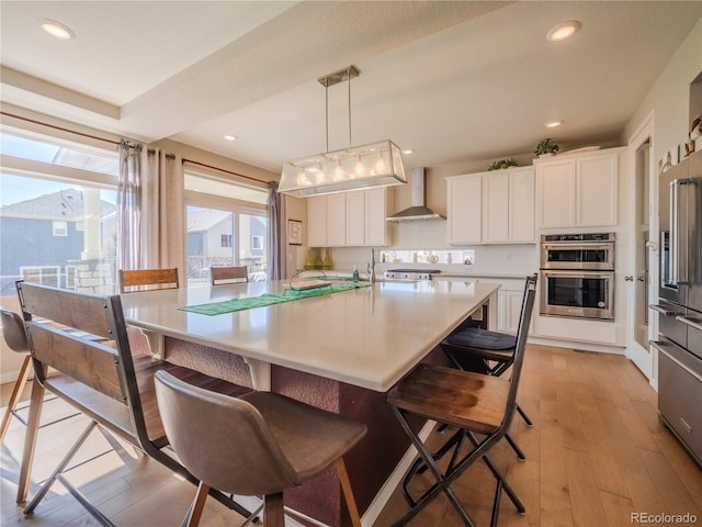 kitchen featuring white cabinets, wall chimney range hood, pendant lighting, and light countertops