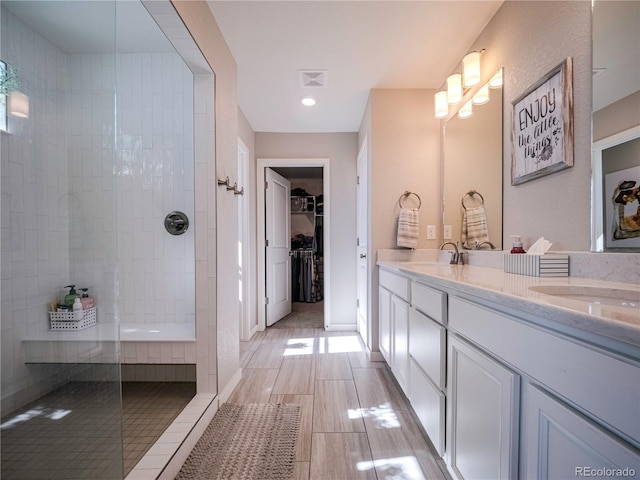 full bath featuring double vanity, visible vents, tiled shower, a walk in closet, and a sink