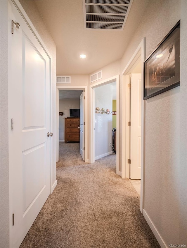 hall featuring light carpet, baseboards, and visible vents