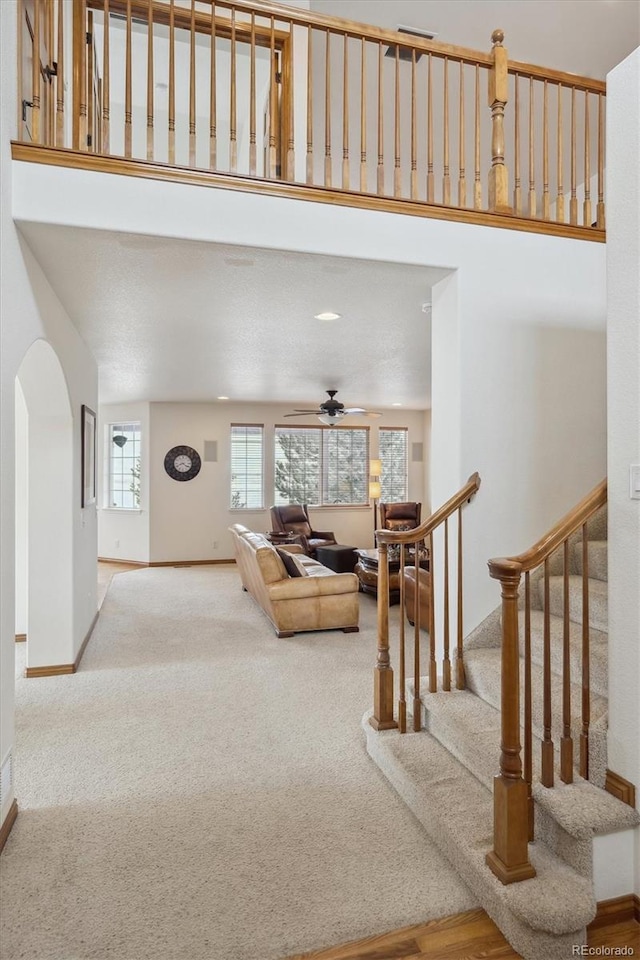 living room featuring baseboards, arched walkways, light colored carpet, ceiling fan, and stairway