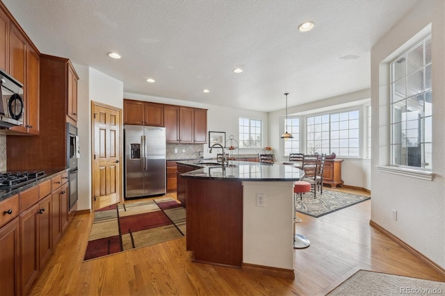 kitchen with an island with sink, a kitchen bar, appliances with stainless steel finishes, and decorative light fixtures