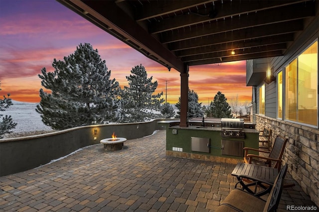 patio terrace at dusk featuring area for grilling, a sink, a fire pit, and an outdoor kitchen