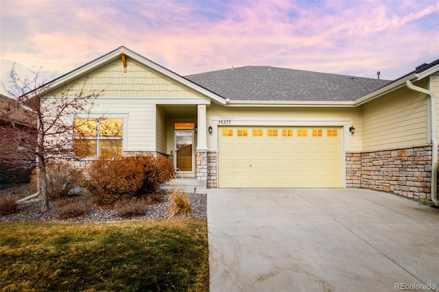 view of front facade with a garage, concrete driveway, a shingled roof, and stone siding