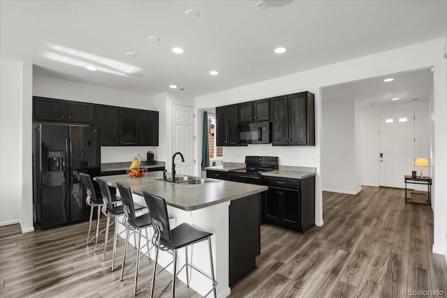 kitchen with sink, a center island with sink, wood-type flooring, black appliances, and a kitchen bar